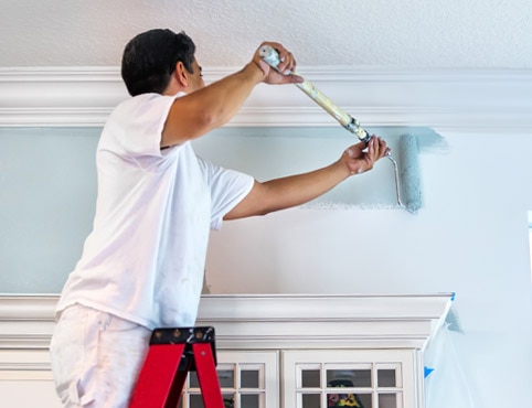 A painting contractor rolls blue paint onto a wall. A painting contractor rolls blue paint onto a wall.